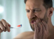 As a man brushes his teeth, he experiences tooth pain, and wonders how to prevent tooth decay
