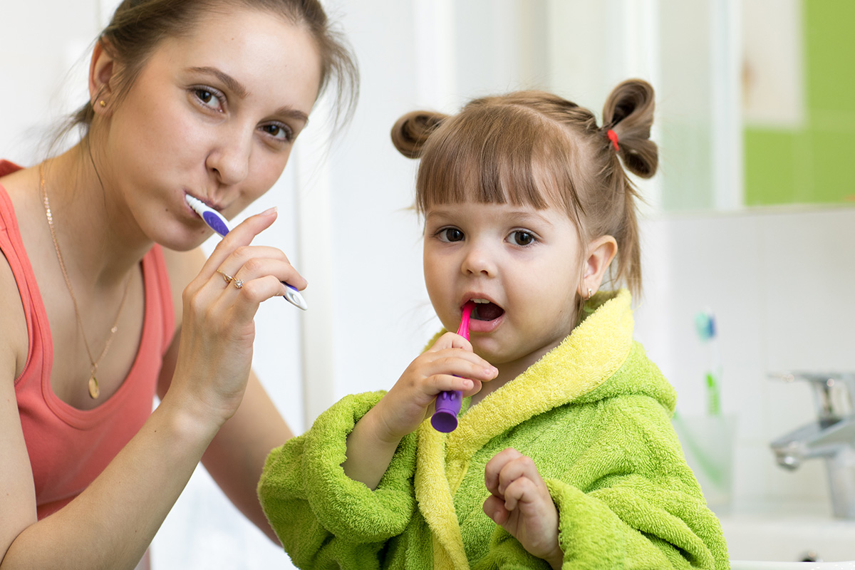 a woman teaches her daughter about preventing sensitive teeth using oral hygiene